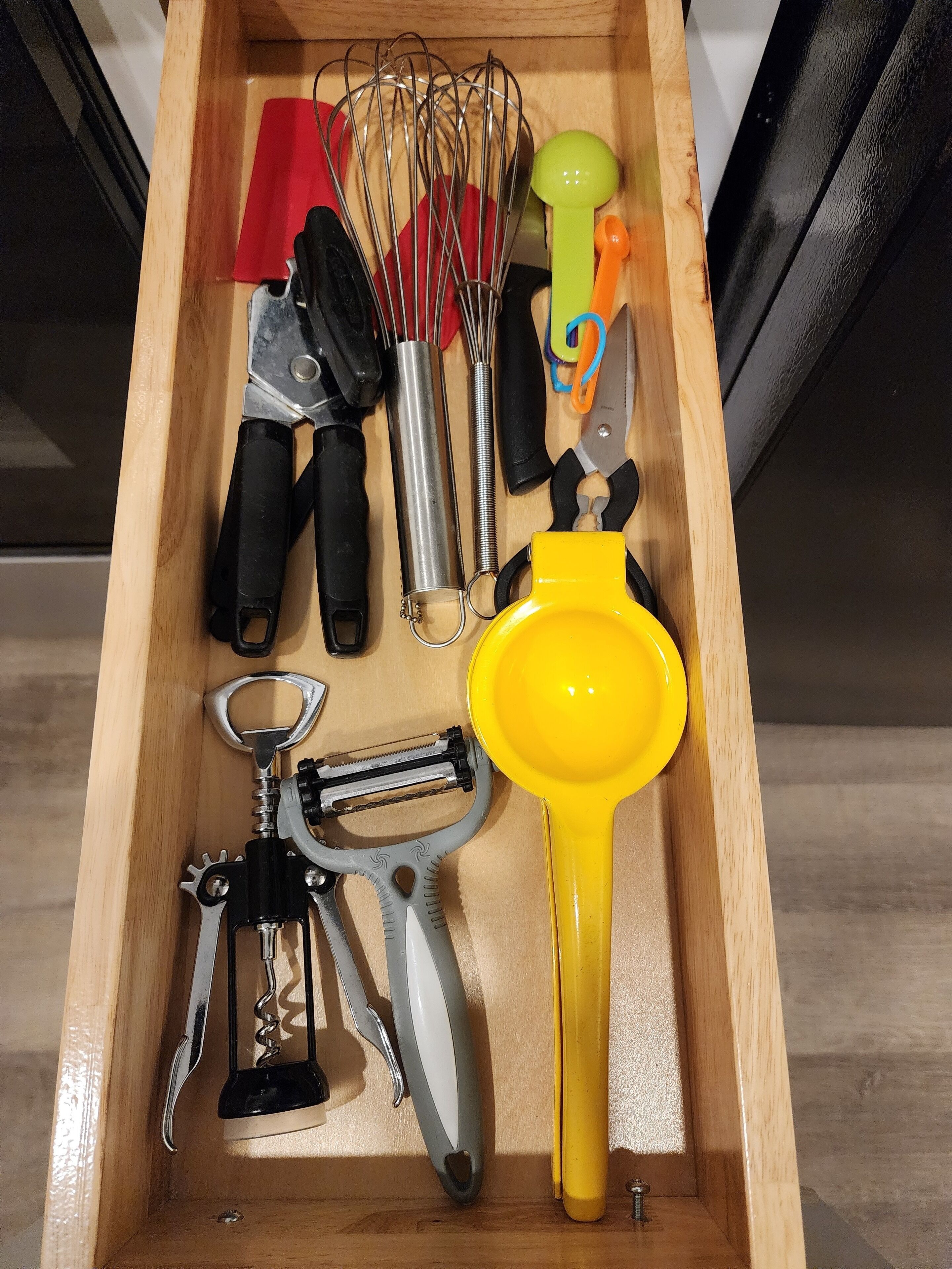 Un cajón con varios utensilios de cocina, incluyendo un batidor, un rallador y un colador amarillo.