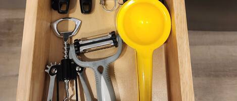 Un cajón con varios utensilios de cocina, incluyendo un batidor, un rallador y un colador amarillo.