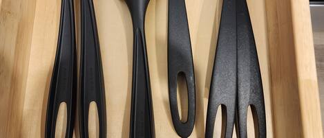 A wooden drawer containing four black kitchen utensils: a spatula, a ladle, and two spoons.