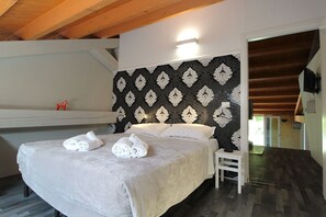 Cama bem arrumada com toalhas, teto de madeira, parede estampada e uma pequena mesa branca.