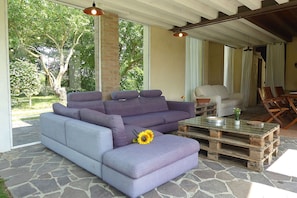 A modern outdoor seating area with a purple sofa, a glass coffee table, and a rustic wooden table. - Nice apartment in villa for 4 people with pool, WIFI, A/C, patio and pets allowed (Cendon)
