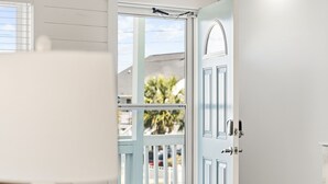 A white door with a window, a white fence, and a view of palm trees and buildings. - 5BR Channel Home w/ Heated Pool + Fire Pit (North Myrtle Beach)