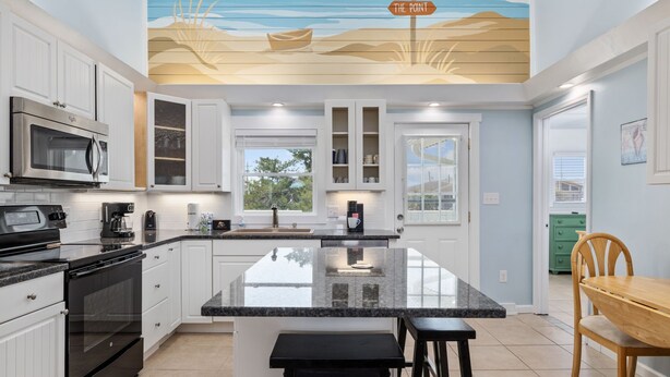 A modern kitchen with white cabinets, a large island, and a beach-themed ceiling mural. - 5BR Channel Home w/ Heated Pool + Fire Pit (North Myrtle Beach)