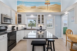 Een moderne keuken met witte kasten, een groot eiland en een plafondschildering met een strandthema.