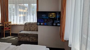 A hotel room with a bed, a chair, a TV mounted on the wall displaying various channels, and a window with curtains. - City Hotel (Boeblingen)