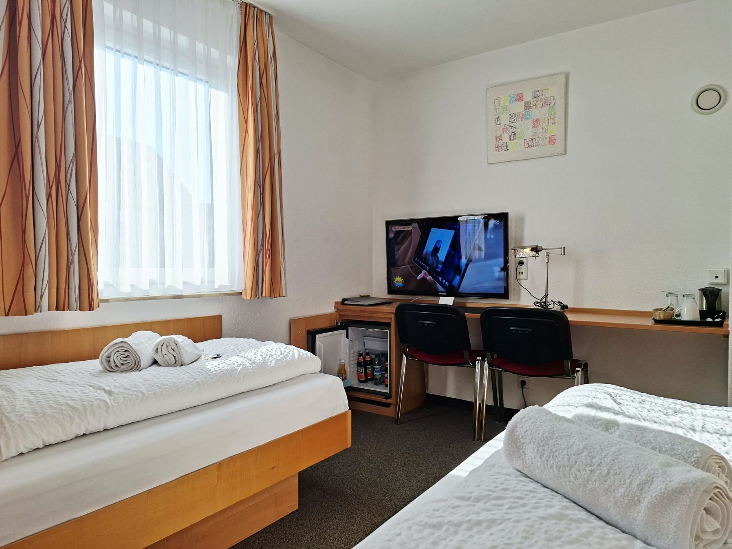 Ein Hotelzimmer mit Bett, Schreibtisch mit Computer, Stuhl und kleinem Kühlschrank.