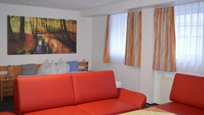 A room with a red sofa, a painting of a forest path, and curtains on the windows. - City Hotel (Boeblingen)