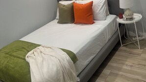 Ein Schlafzimmer mit Bett, Kissen, einem Nachttisch mit Lampe und einem Fenster mit Jalousien.
