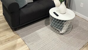 Ein modernes Wohnzimmer mit einem schwarzen Sofa, einem weißen Couchtisch und einem grauen Teppich.