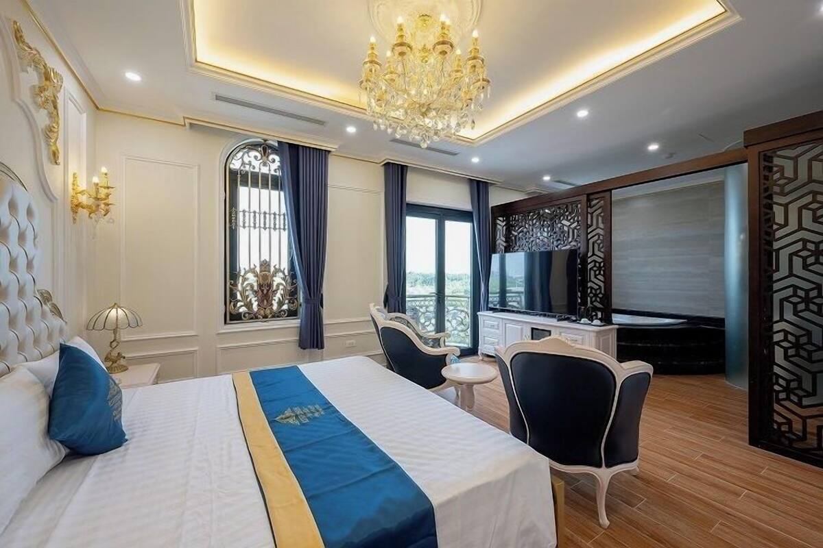 A hotel room with a large bed, a chandelier, a television, and a balcony view.