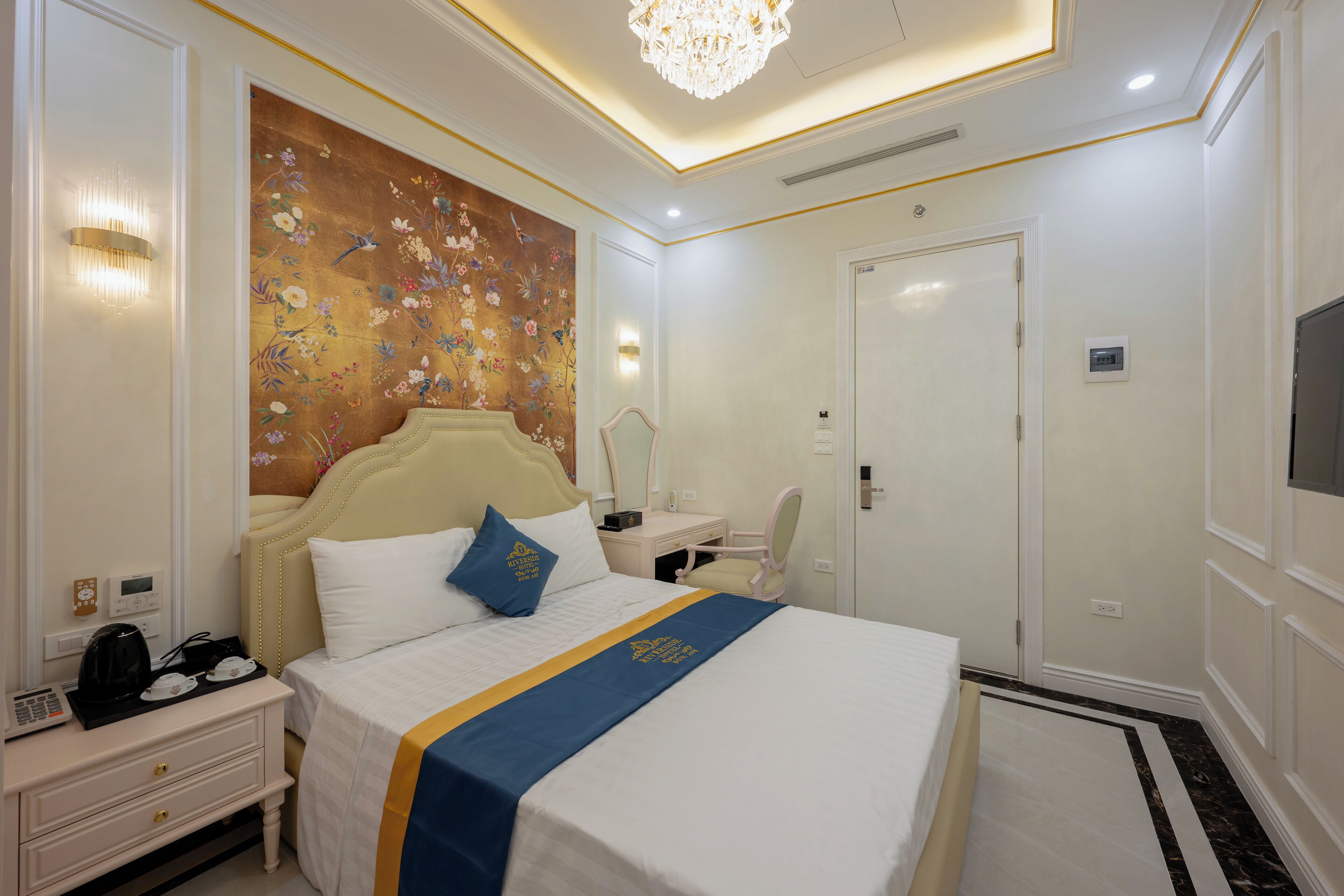 Habitación de hotel con una cama grande, una mesita de noche, un escritorio, una silla, un televisor y un adorno en la pared.