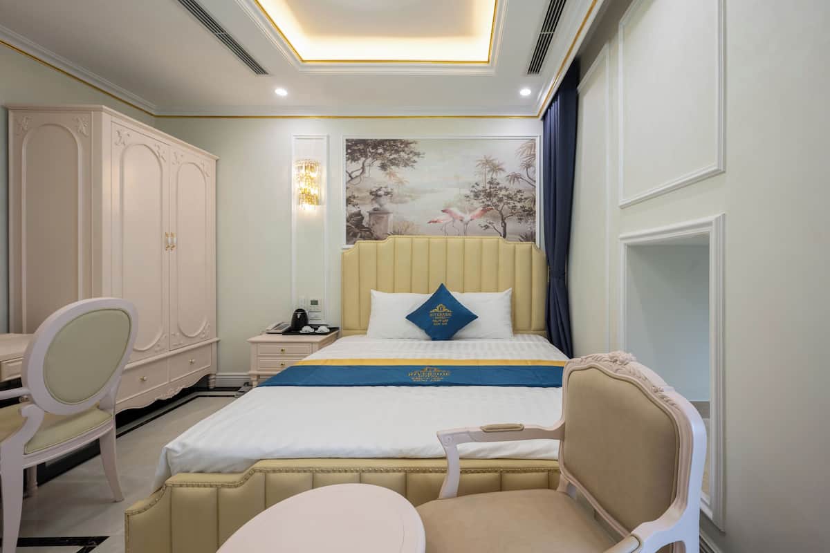 A hotel room with a large bed, a desk, a chair, and a nightstand.