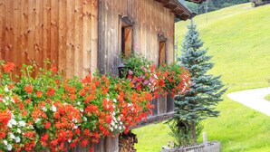 En træchalet med en balkon pyntet med blomstrende blomster, med udsigt til en grøn skråning og en klar himmel.