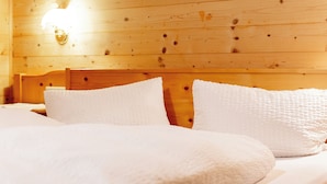 A wooden cabin bedroom with a bed, pillows, and a wall-mounted light fixture.