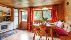 A wooden cabin interior with a kitchen, dining area, and a window with curtains.
