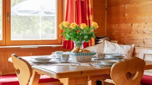 A wooden dining table with a vase of yellow roses, red curtains, and a window with a view of trees. - Two big alpine stays for families & groups (Alpbach)