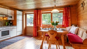 A cozy cabin-style kitchen with wooden walls, a dining table, and a red bench. - Two big alpine stays for families & groups (Alpbach)