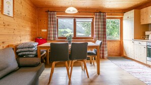 A wooden cabin interior with a dining area, kitchen, and a sofa. - Two big alpine stays for families & groups (Alpbach)