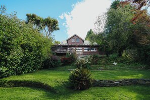 Ein Haus mit einer Holterrasse, umgeben von üppiger Bepflanzung und einem gepflegten Rasen.