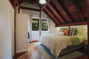 Ein Schlafzimmer mit Holzboden, einem Bett mit vielen Kissen, einem Nachttisch und einem Fenster mit Vorhängen.