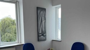 Een kamer met twee blauwe stoelen, een kleine ronde tafel, een schilderij aan de muur en een raam met uitzicht op bomen.