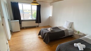 Een kamer met twee bedden, een raam met gordijnen, een radiator en een houten plafond.