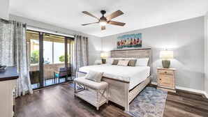 A bedroom with a large bed, a ceiling fan, a bench, a nightstand, and a painting on the wall.