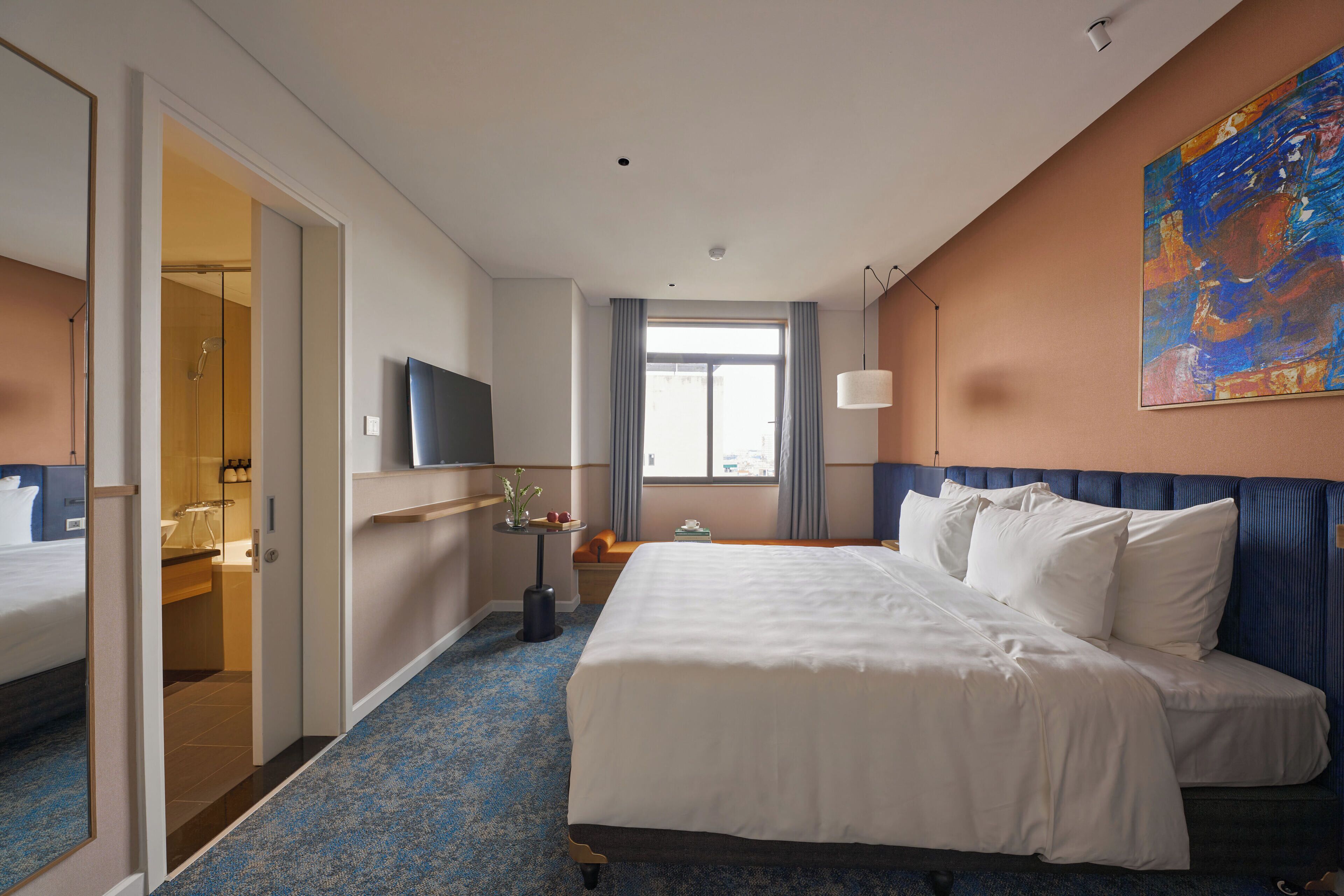 Habitación de hotel con una cama grande, televisión, ventana con cortinas y un cuadro en la pared.
