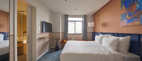 Habitación de hotel con una cama grande, televisión, ventana con cortinas y un cuadro en la pared.