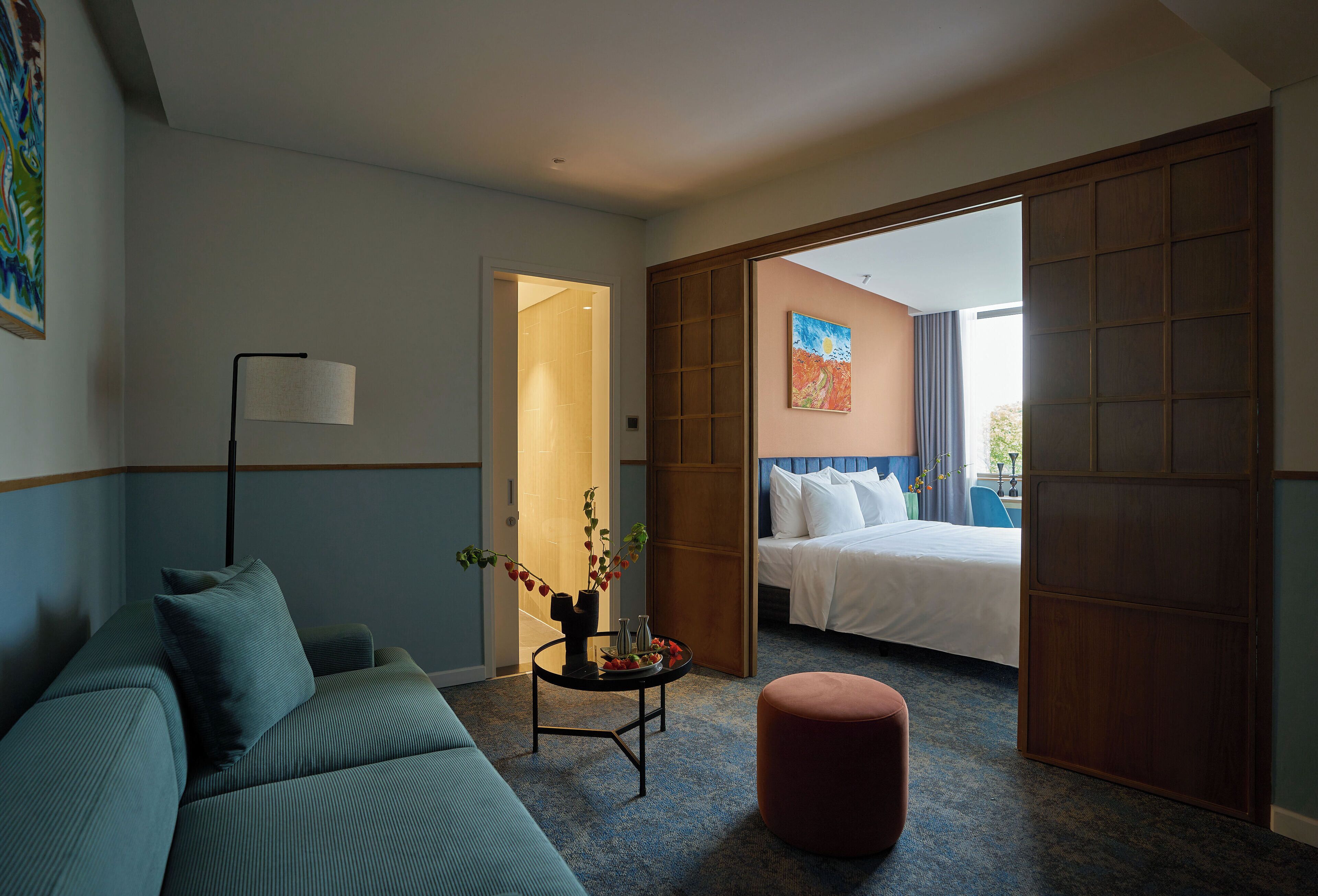 A hotel room with a bed, a sofa, a small table with a vase, and a view of the outside.