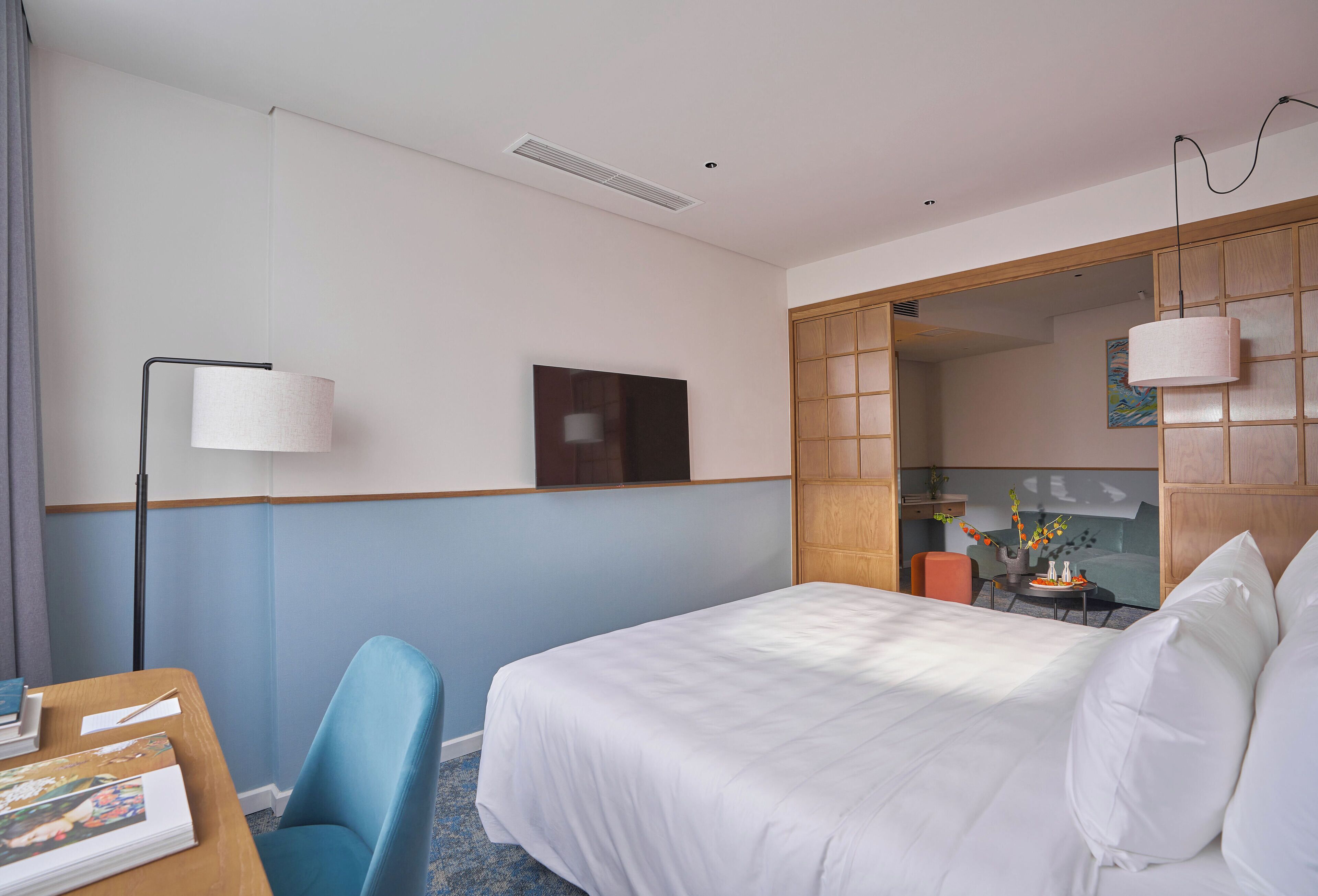 A hotel room with a bed, a desk with a chair, a lamp, and a television.