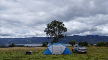 A camping site with a tent, a car, and a tree.