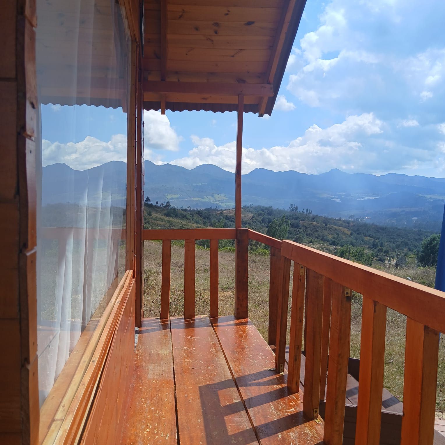 A wooden balcony with a view of mountains and a clear sky.