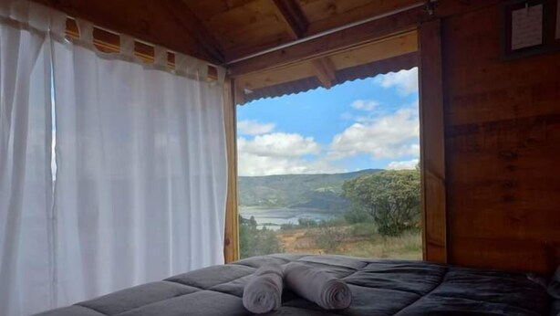 Un dormitorio con un ventanal grande, una cama con colcha oscura y vistas a un paisaje.