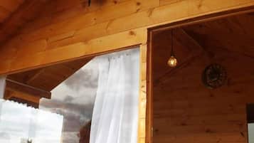 Une pièce de style cabane en bois, avec un lit, une fenêtre avec des rideaux, une horloge murale et un luminaire suspendu.