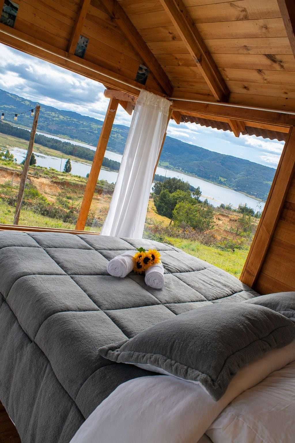 Un lit donnant sur un lac et des montagnes, un plafond en bois et un rideau.