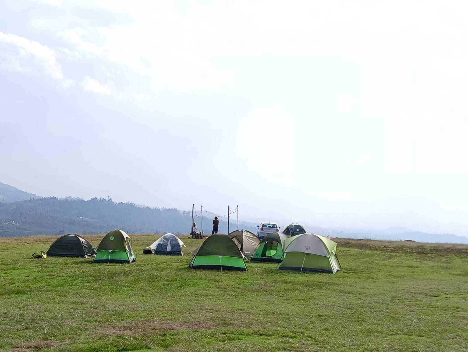 A campsite with several tents set up on a grassy field, with a hilly landscape in the background.
