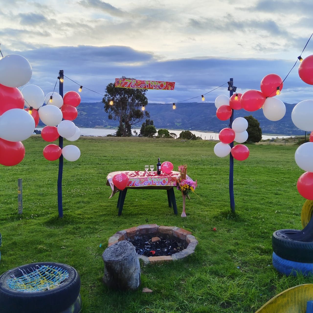 Un entorno al aire libre con una mesa preparada para una celebración, un hogar para fuego y una vista panorámica al fondo.