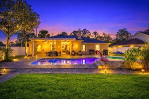 Una casa con piscina, mobiliario exterior y un patio bien iluminado.