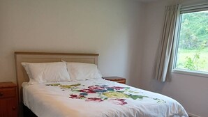 Un dormitori amb un llit, una tauleta de nit, un armari de fusta i una finestra amb cortines.