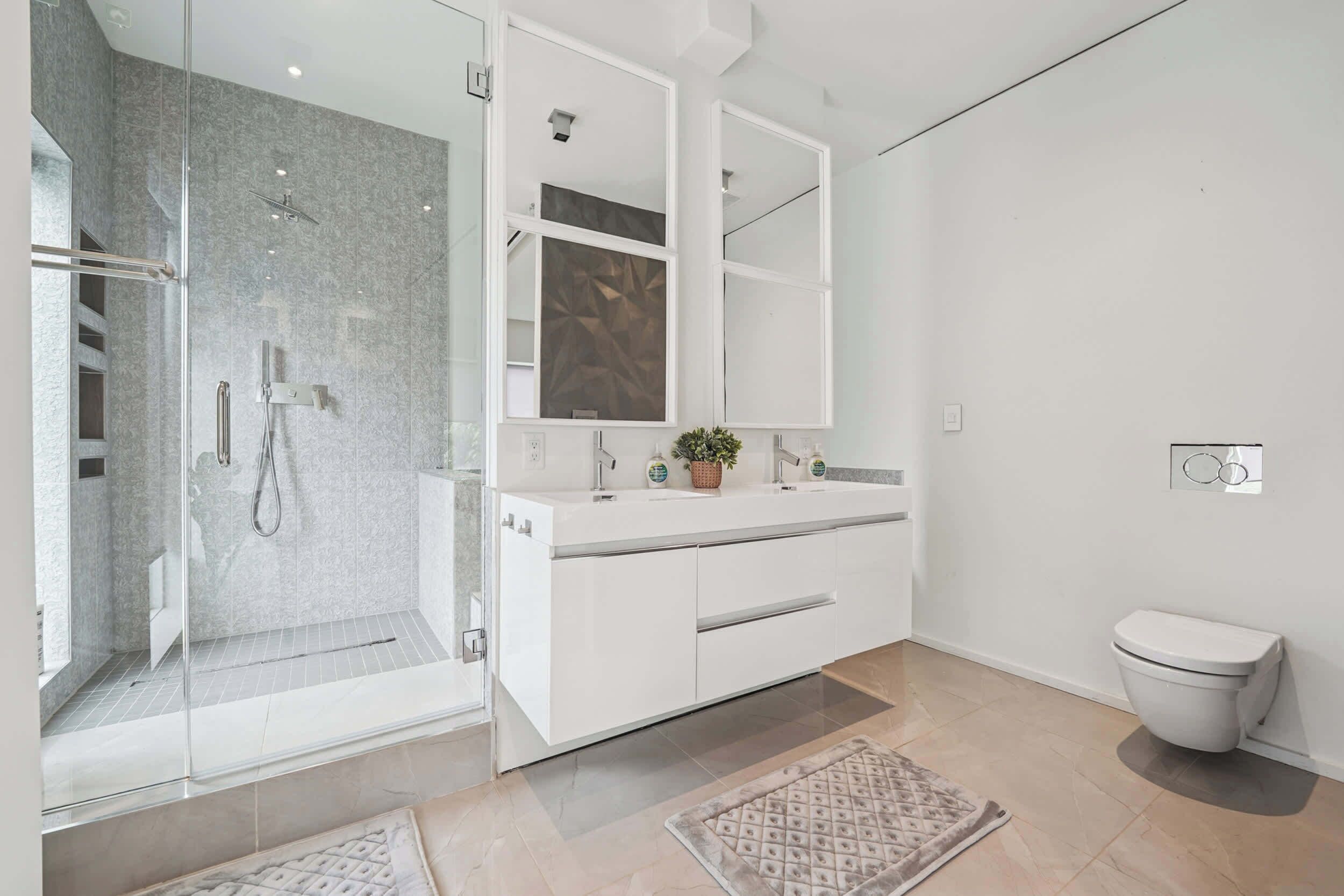 Een moderne badkamer met een douchecabine van glas, een wit wastafelmeubel met spiegel, en een toilet.