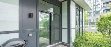 A modern building with large glass doors, a small outdoor seating area, and a well-maintained garden.