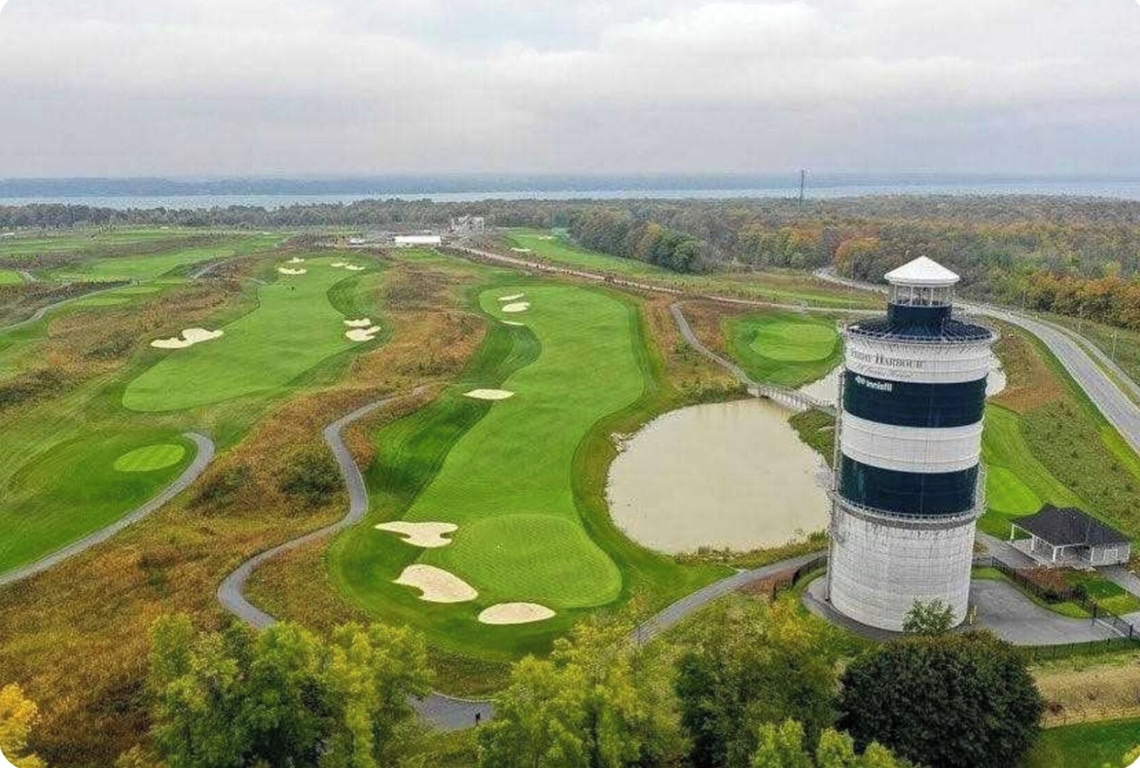 Um campo de golfe com bunkers, áreas de água e uma estrutura semelhante a um farol.