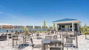 Une terrasse sur le toit avec des espaces de détente en plein air, un coin barbecue et une vue sur un port de plaisance et des immeubles.