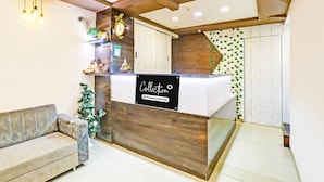 A reception area with a wooden reception desk, a sofa, and a wall-mounted clock. - Collection O Palampur Surat (Surat)