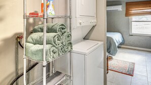 Un área de lavandería con lavadora, un tendedero con toallas dobladas y una cama con vistas a la ventana.