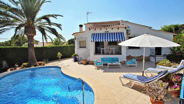 A pool area with a palm tree, lounge chairs, and a building with a striped awning. - Azahar - villa with privat pool in Moraira (Moraira)