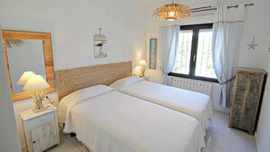 A bedroom with two beds, a nightstand with a lamp, a wall-mounted mirror, and a window with curtains. - Azahar - villa with privat pool in Moraira (Moraira)