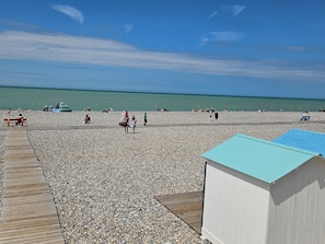 A pebble beach with a wooden walkway and a small building with a blue roof.