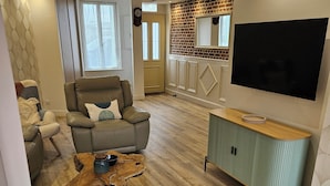 Un salon moderne comprenant un canapé, un fauteuil, une table basse et un téléviseur fixé au mur.